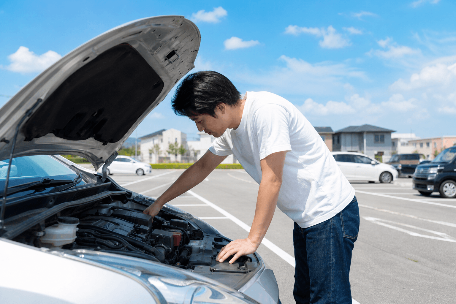 夏の晴れた日、駐車場でボンネットを開けて自分の車のエンジンルームを確認している男性