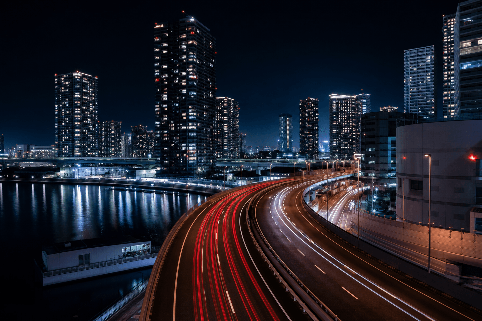 Light trails streaking along an elevated Tokyo bayside expressway between high-rise towers at night