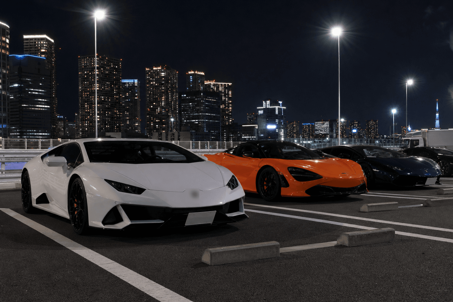 Supercars parked at a Tokyo expressway parking area at night with the city skyline glowing behind them
