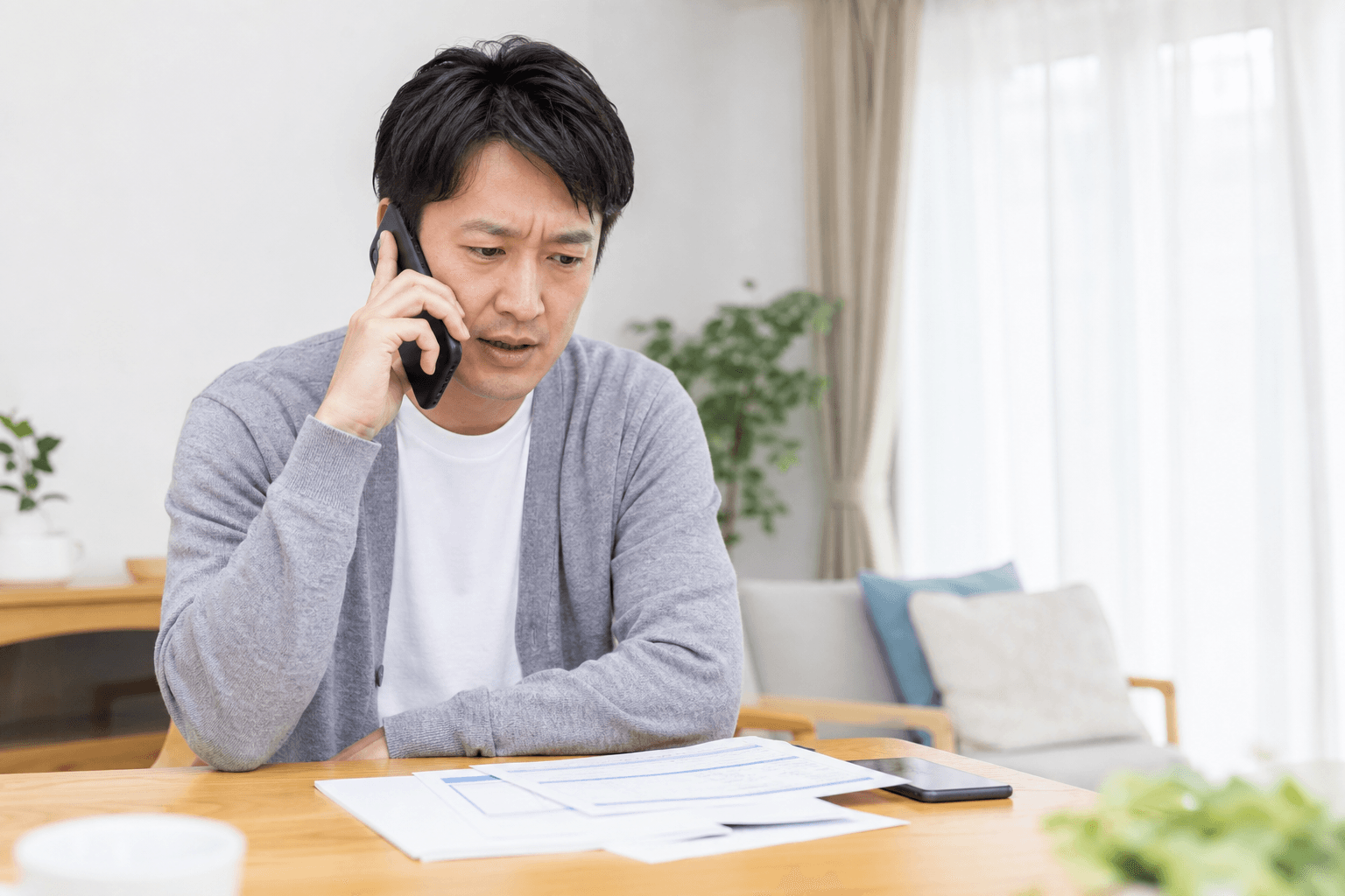 自宅で保険の書類を前に、電話で保険会社と話している男性