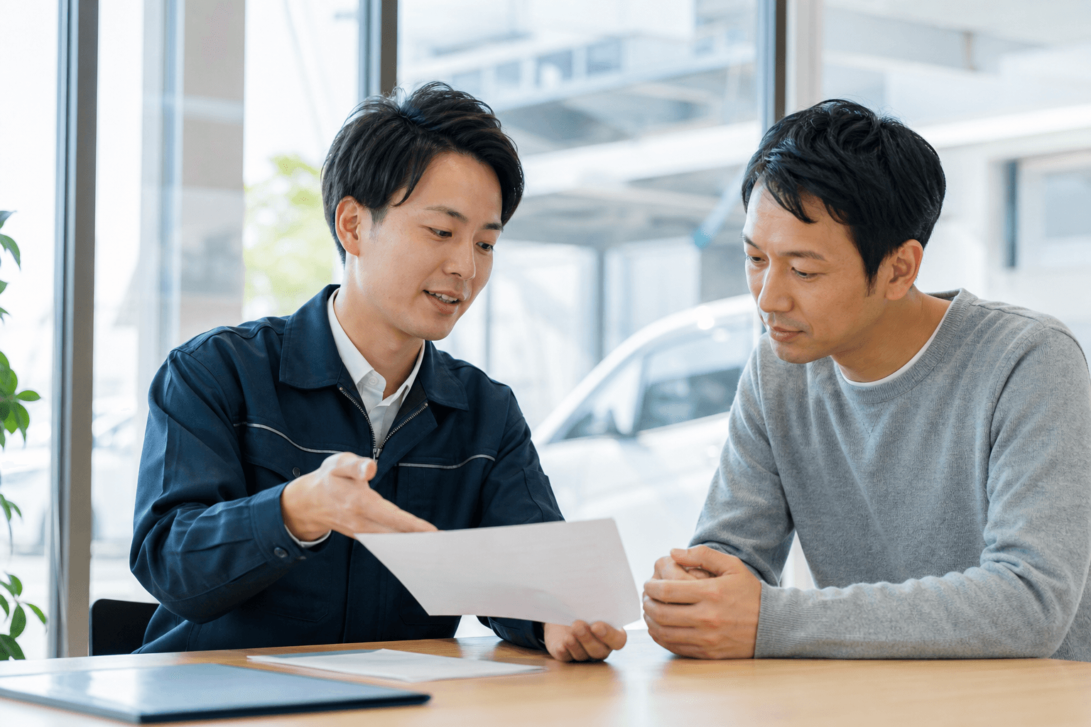 自動車店の相談カウンターでスタッフが顧客に書類を見せながら説明する場面
