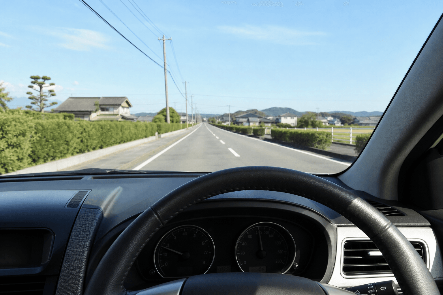 運転席から見たハンドルと、まっすぐ続く郊外の道路