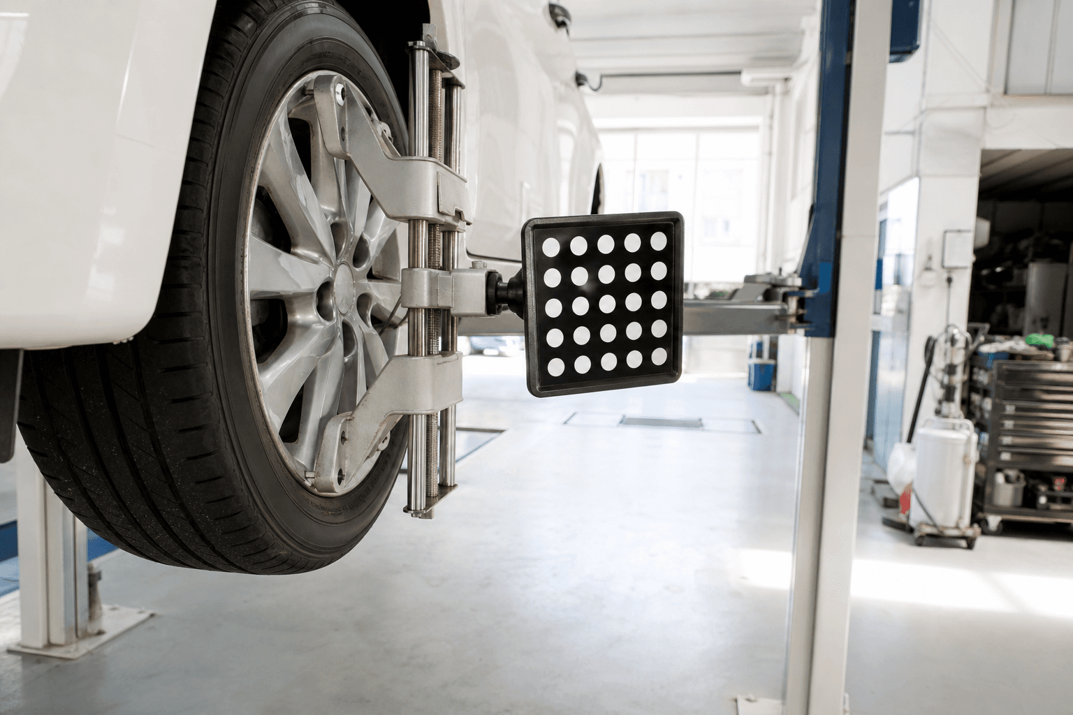 明るく清潔な整備工場で、リフトに上げた車のホイールにアライメント測定用のセンサーを取り付けた様子