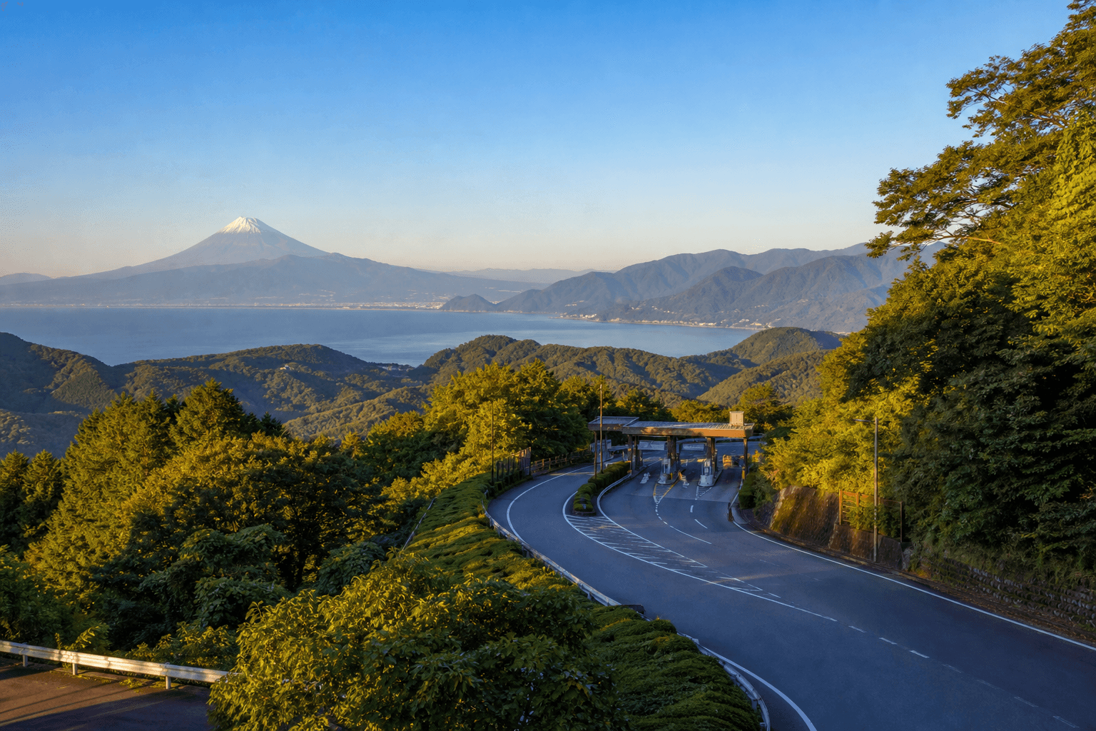 A winding mountain road climbing toward a view of Mt. Fuji and Sagami Bay